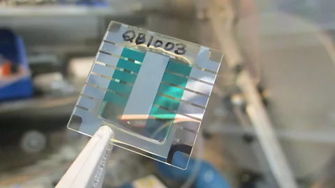 Csiro A close up of a quantum battery: a square transparent plate with a number 2B1003 handwritten on it, held by clippers (Credit: Csiro)