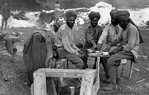 Indian soldiers wearing traditional turbans relax around a makeshift dinner table