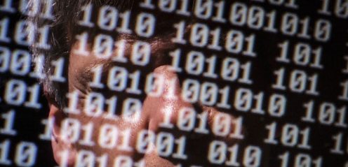 Man's face reflected on computer screen showing binary numbers
