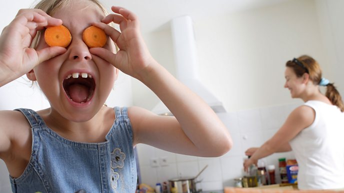 A child holds up chopped carrots to her eyes