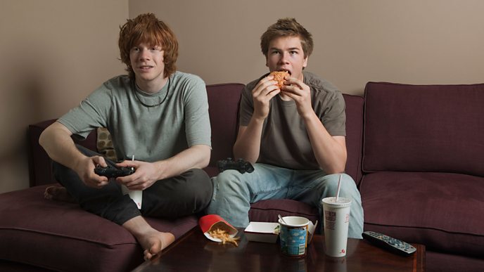 Two teenagers eat junk food while playing a computer game