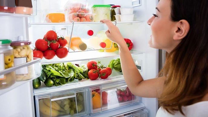 Woman looking in fridge with lots of fruit and vegetables.