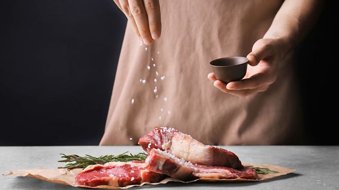 Woman sprinkling salt onto red meat.