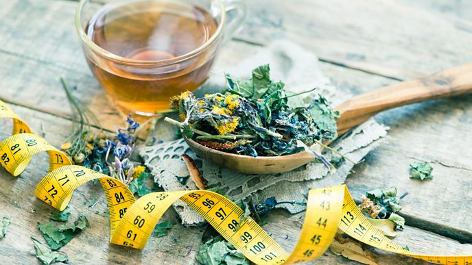 A picture of tea with herbs/plants on a spoon next to it and a tape measure