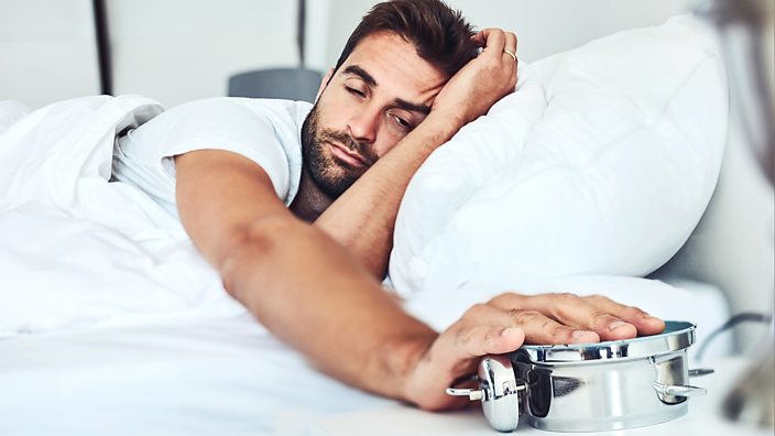 A photo of a man turning over his alarm clock so he can stay in bed