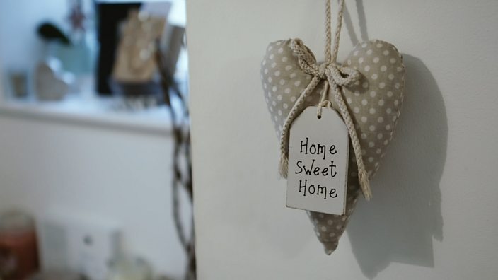 A trinket with the word 'home sweet home' hangs from a door in Alex's family home