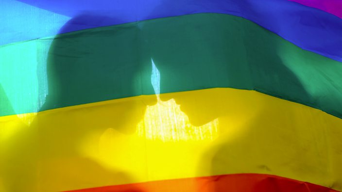 A lesbian couple silhouetted behind a rainbow flag