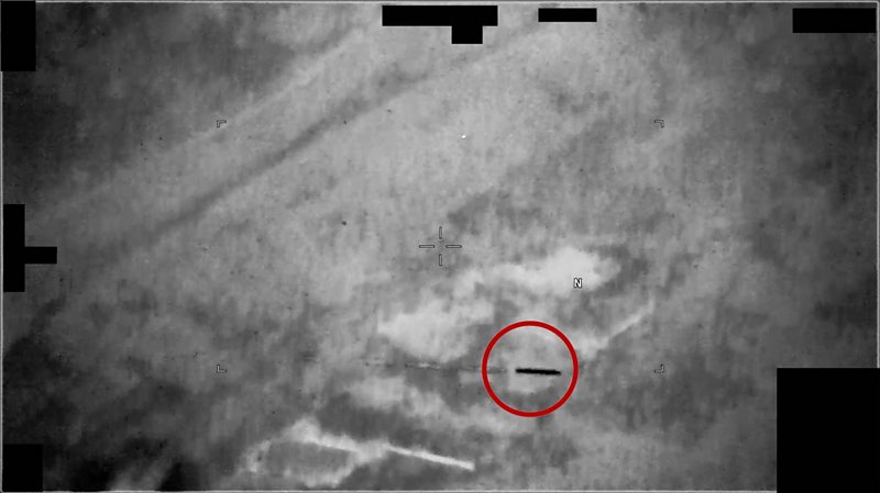 An unidentified black, tubular thing shoots through the air. There is a red ring around it.