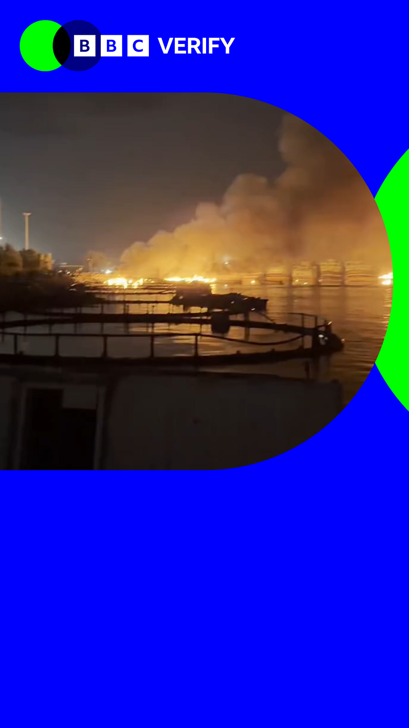 far away view of a burning harbour at night with BBC Verify branding colours