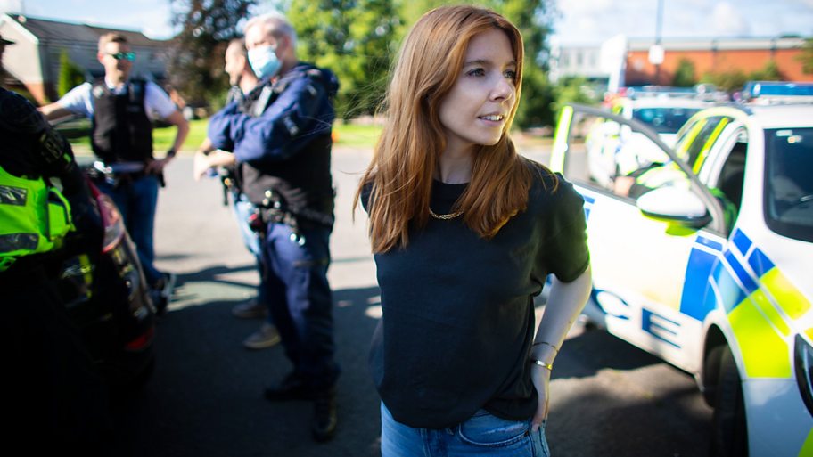 Stacey Dooley standing next to a police car