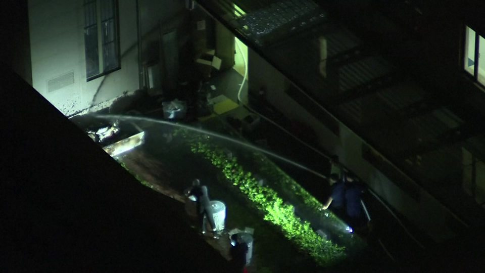 mężczyźni są filmowani za pomocą węża i zamykania koszy na śmieci w konsulacie Chin w Houston's consulate in Houston