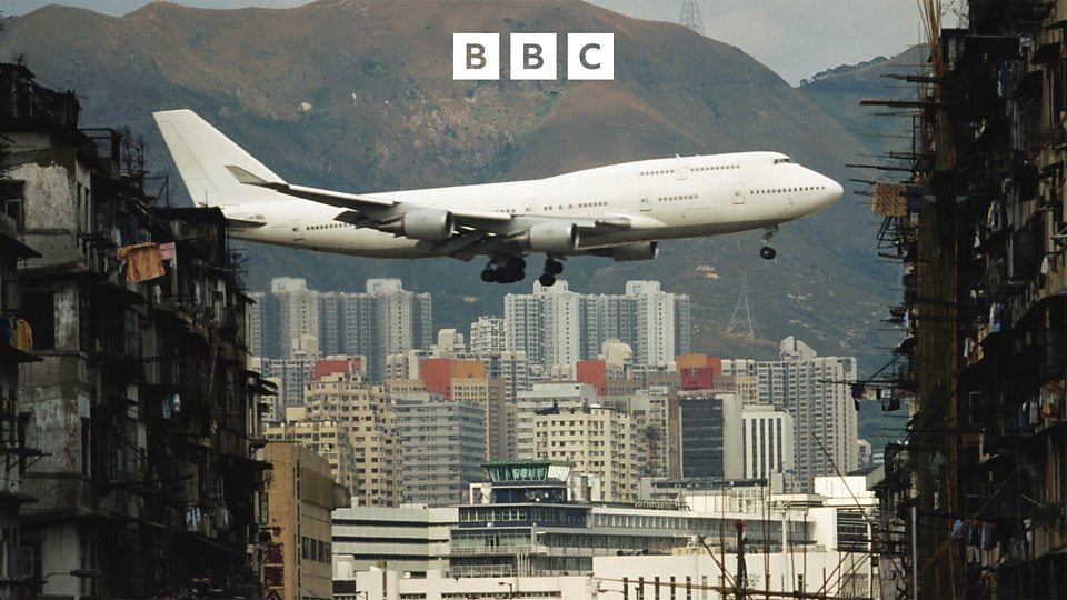 A plane going in for landing with slum-like buildings in the foreground.