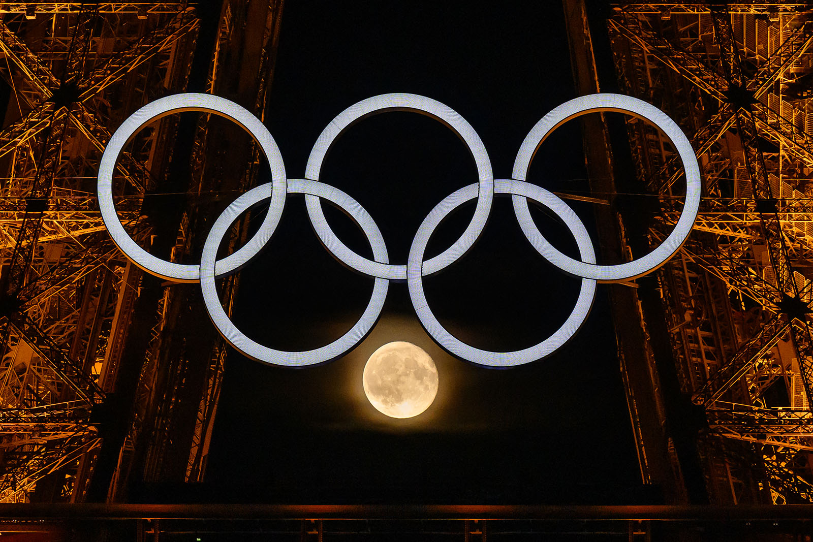 The moon is pictured through the Olympic rings displayed on the Eiffel tower 