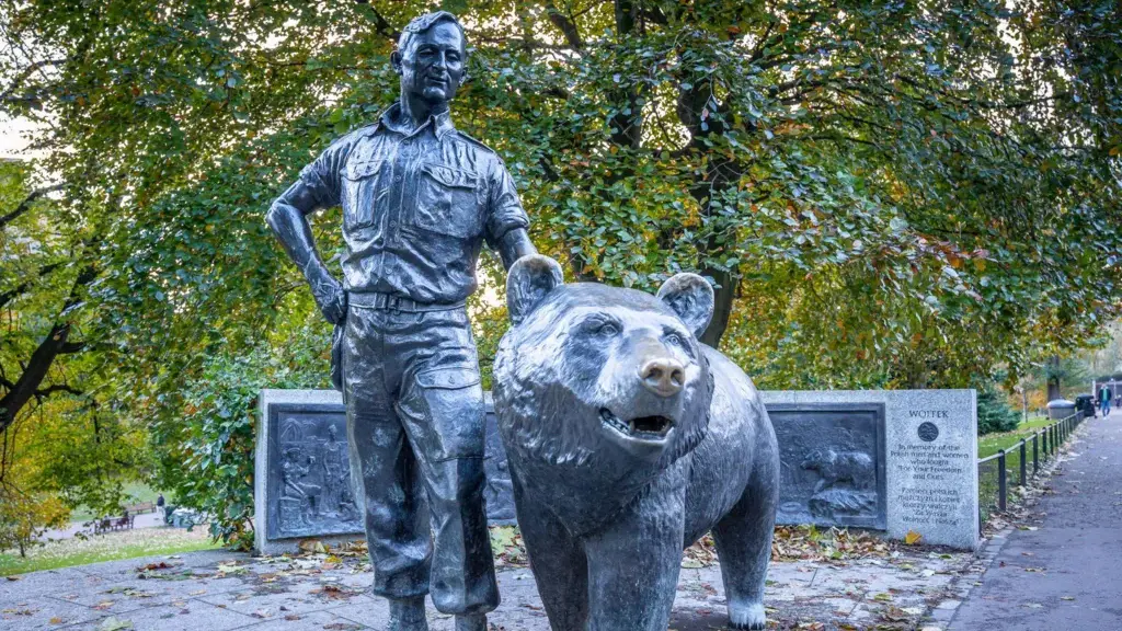 A beret-wearing Polish Army soldier throws food into the mouth of Wojtek, a Syrian brown bear which is wearing a collar and chain