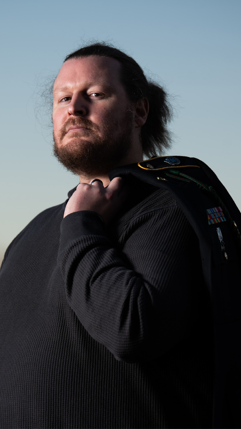 John Doty poses holding a military jacket with medals.