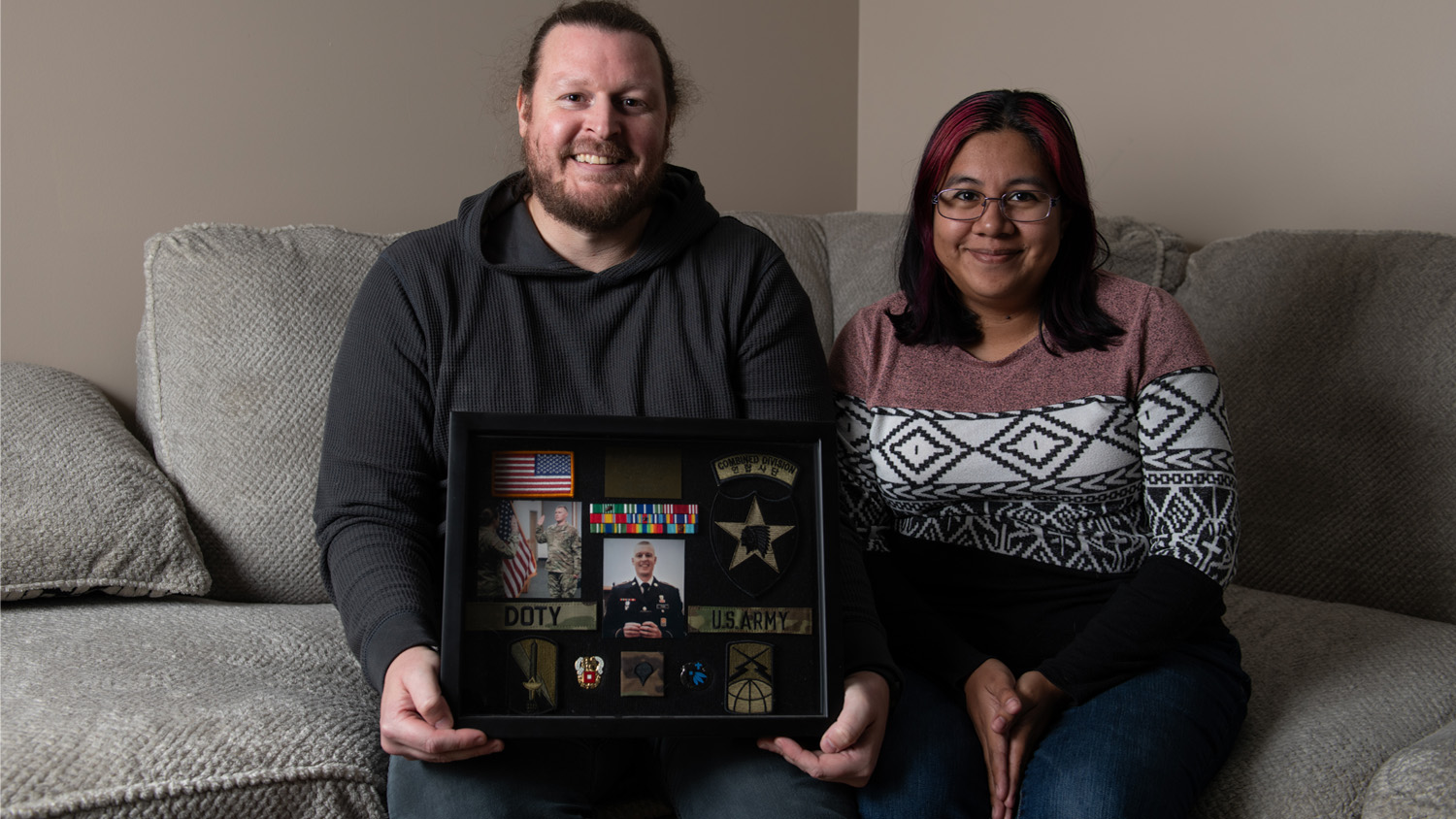 John Doty poses side by side with a woman while he holds a frame with memorabilia from his military service.