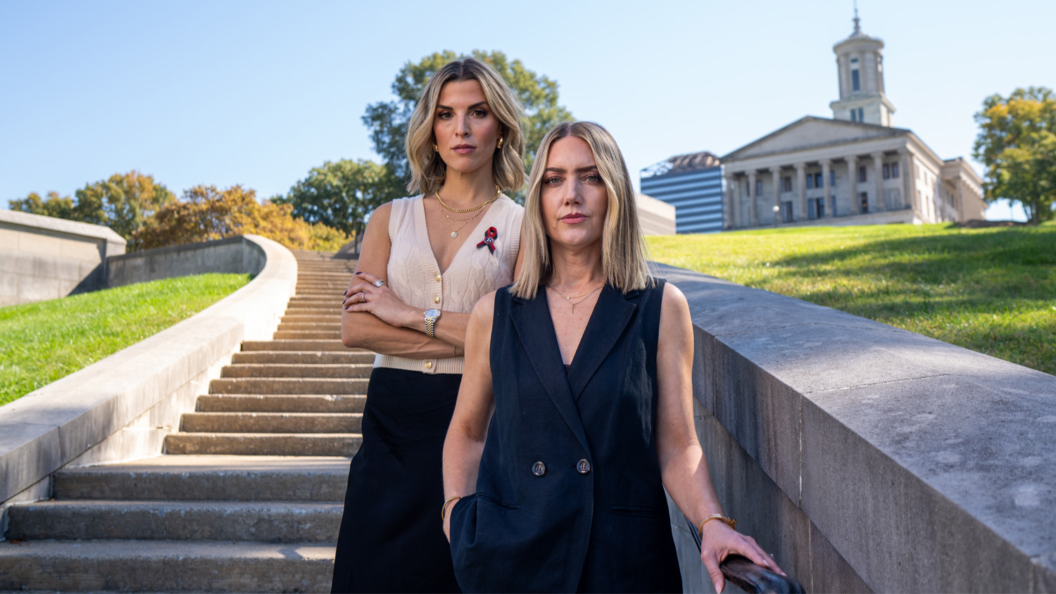 Mary Joyce, with arms crossed, and Melissa Alexander, with a hand in her pocket, pose in front of stairs.