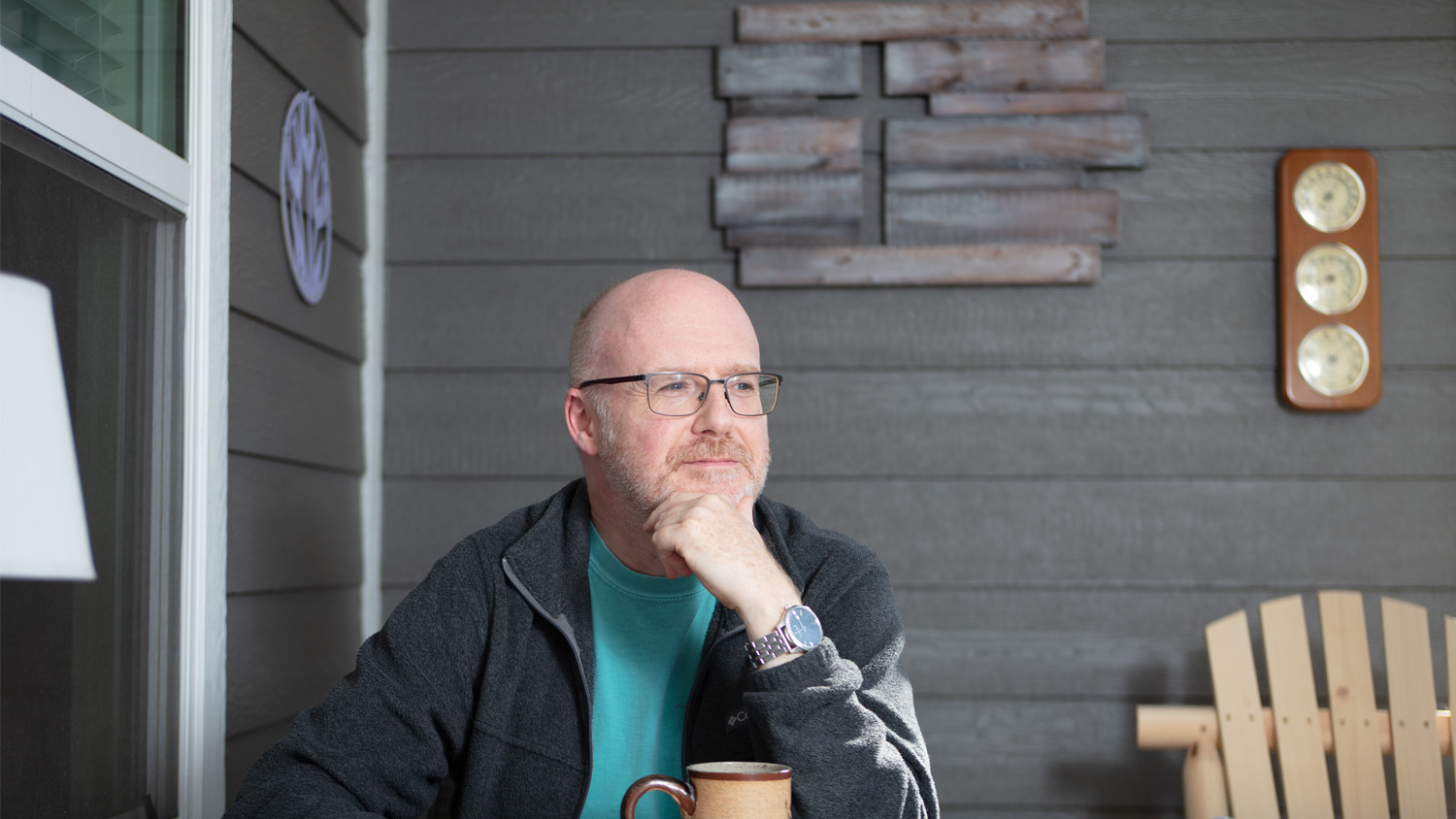 Ric Morris poses with a coffee mug at a table in his terrace. Behind him is a wooden cross.