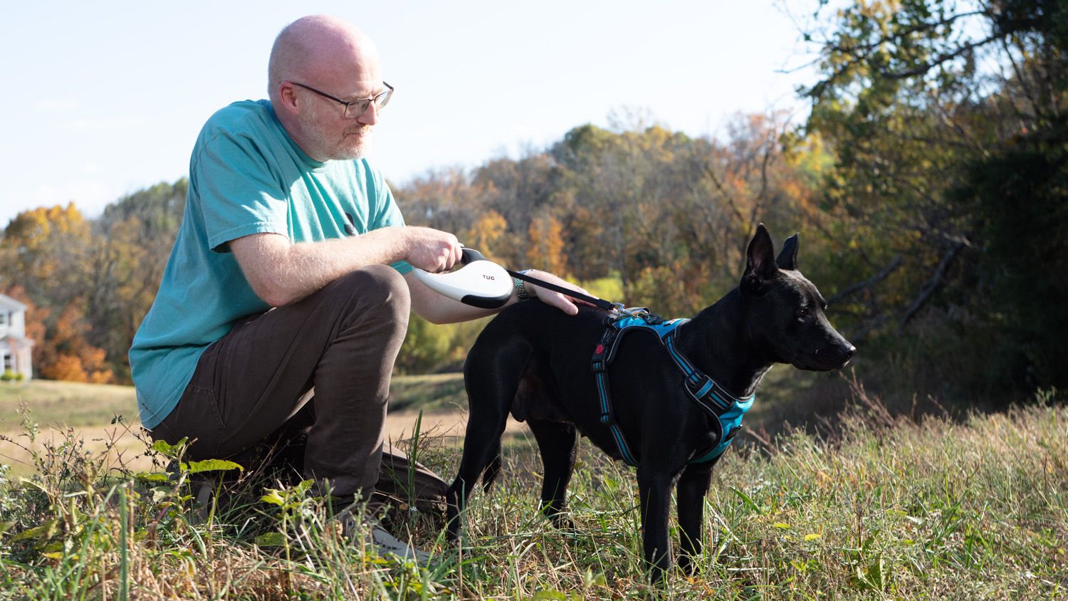 Ric Morris poses in a garden with his dog. He is squatting and stroking his dog.