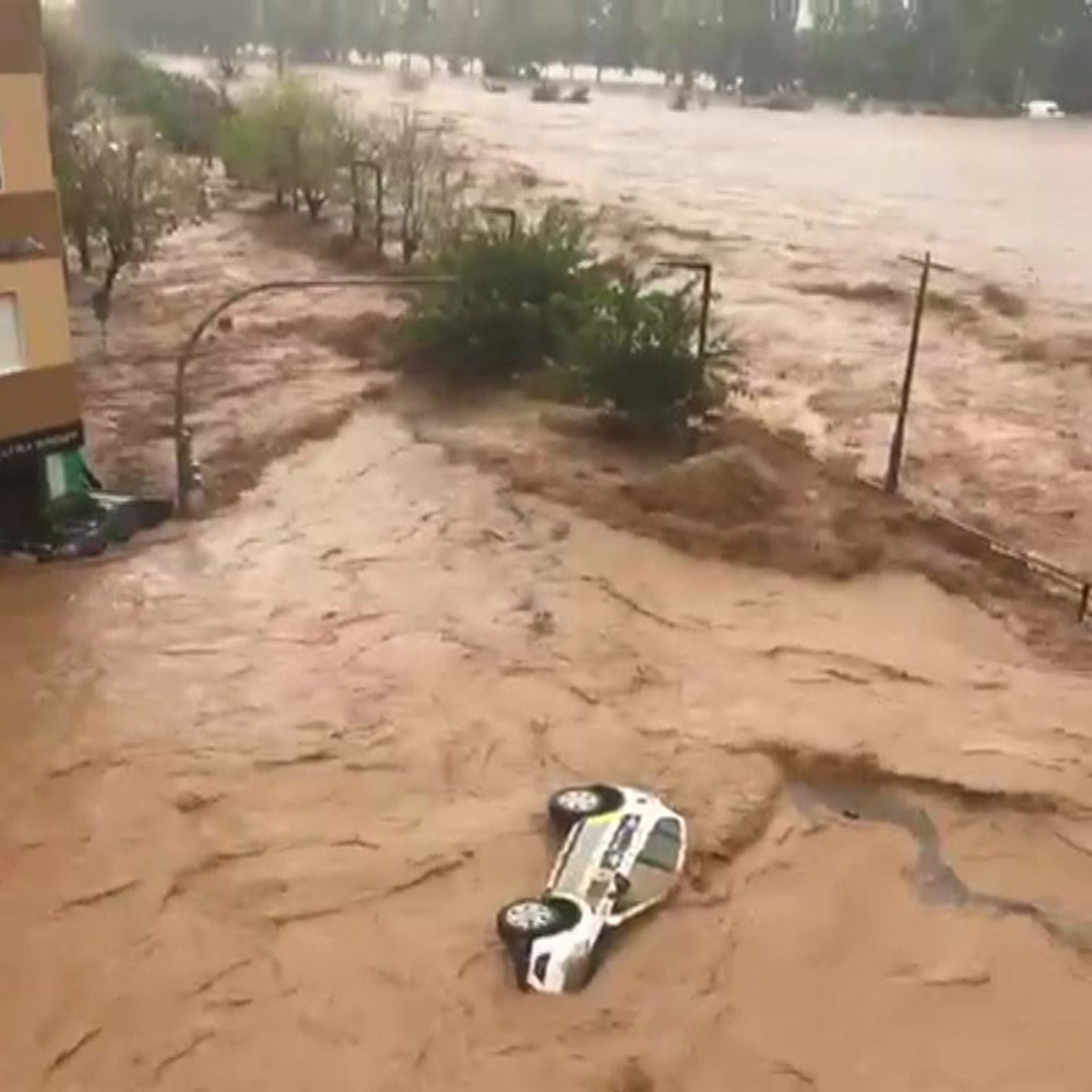 Police car on its side being washed away by the muddly floodwater