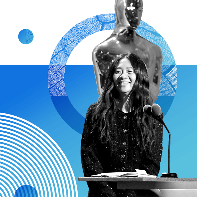 Oscar-winning film director Chloé Zhao with long and wavy hair standing on a stage behind a podium with a microphone. There is a giant Oscar statue behind her.