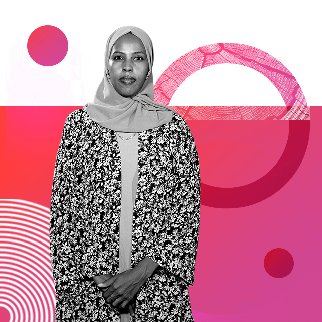 Journalist Hinda Abdi Mohamoud looking straight ahead, wearing a headscarf and a loose fitting floral robe and necklace, clutching her hands in front of her.