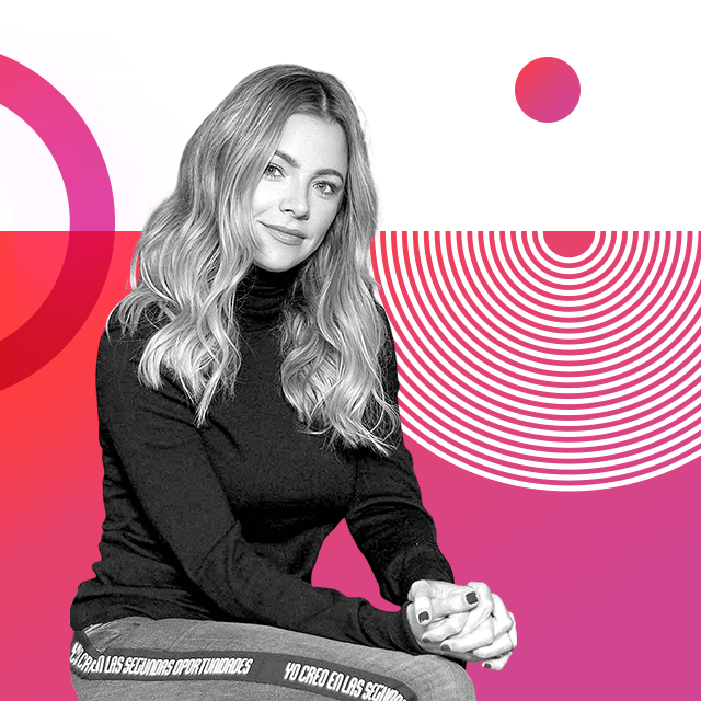 Johana Bahamón with long blonde hair, posing while sitting and wearing a high-neck jumper and jeans with the inscription “I believe in second opportunities” in Spanish.