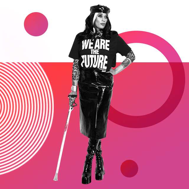 Disability rights advocate Roxy Murray, standing with a walking stick, wearing long leather boots, a hat, and a leather skirt, along with a black T-shirt with the sentence “We are the future” printed on it.