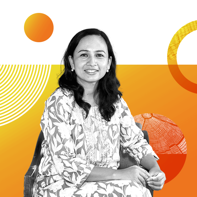 Sustainability entrepreneur Shilshila Acharya is sitting smiling at the camera and wearing a floral dress and pearl earrings.