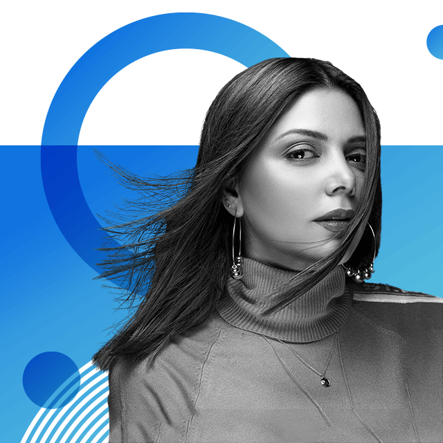 Singer Hadiqa Kiani, with dark windswept hair and wearing a high neck sweater and hoop earrings, is looking at the camera with one lock of hair styled across the left side of her face.