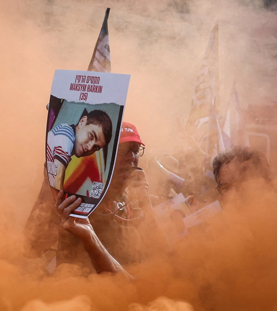 A protester surrounded by smoke from a flare holds up a poster, featuring a 7 October hostage on a Day of Disruption by anti-government protest groups in Shoresh, Israel May 20 2024