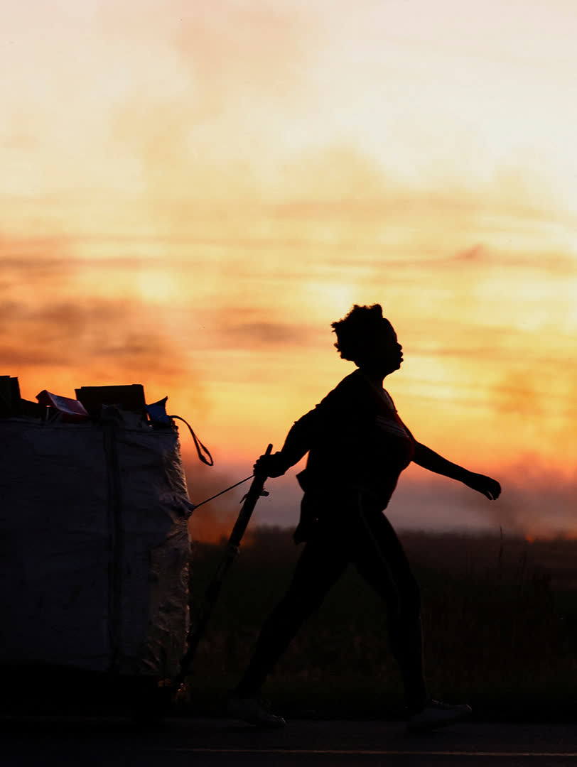 A woman pulls a trolley with recyclable material past veld fires occurring as winter approaches, in Lenasia in the south of Johannesburg, South Africa, April 22, 2024. 