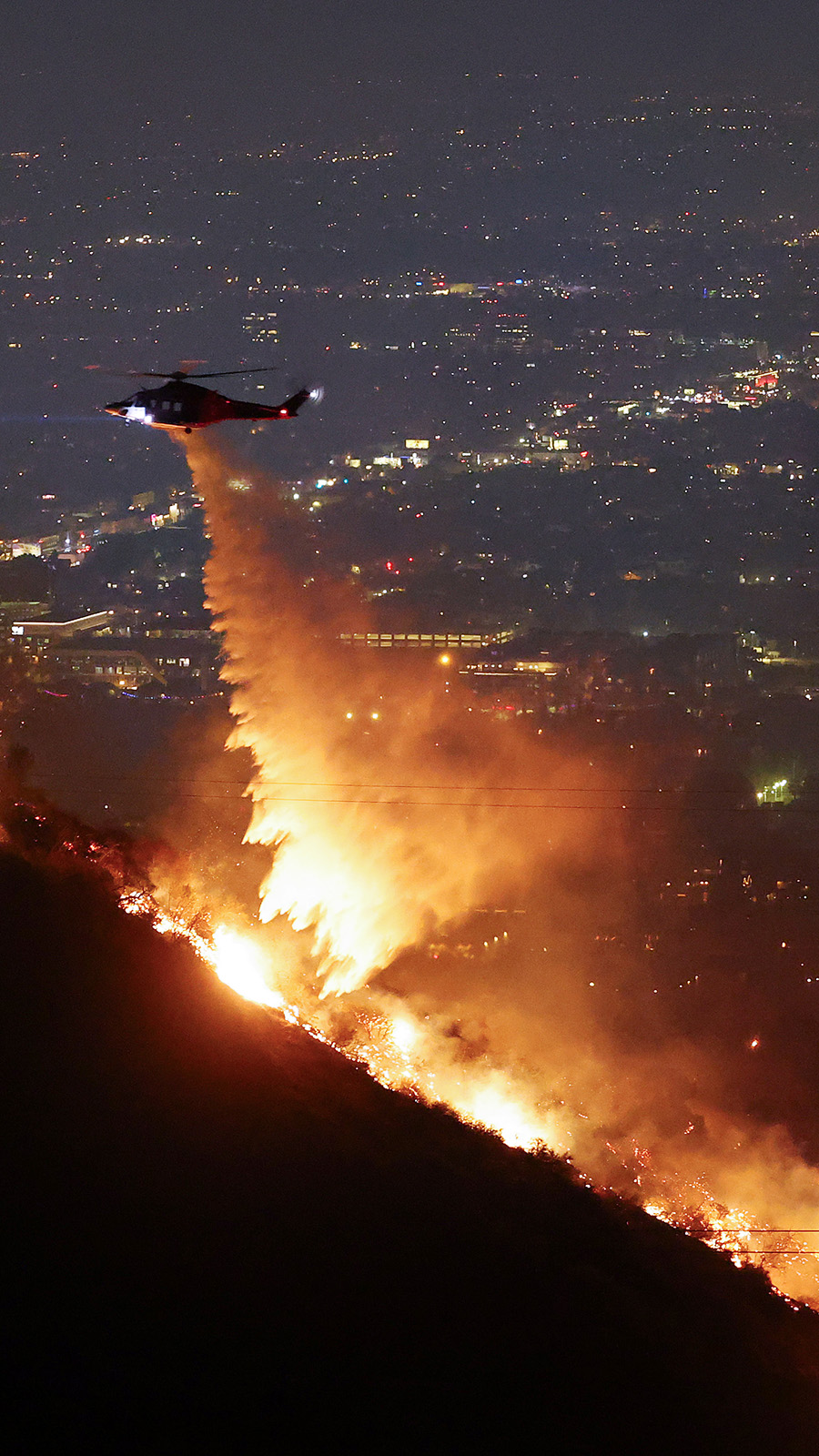 A firefighting helicopter drops water as the Sunset Fire burns in the Hollywood Hills