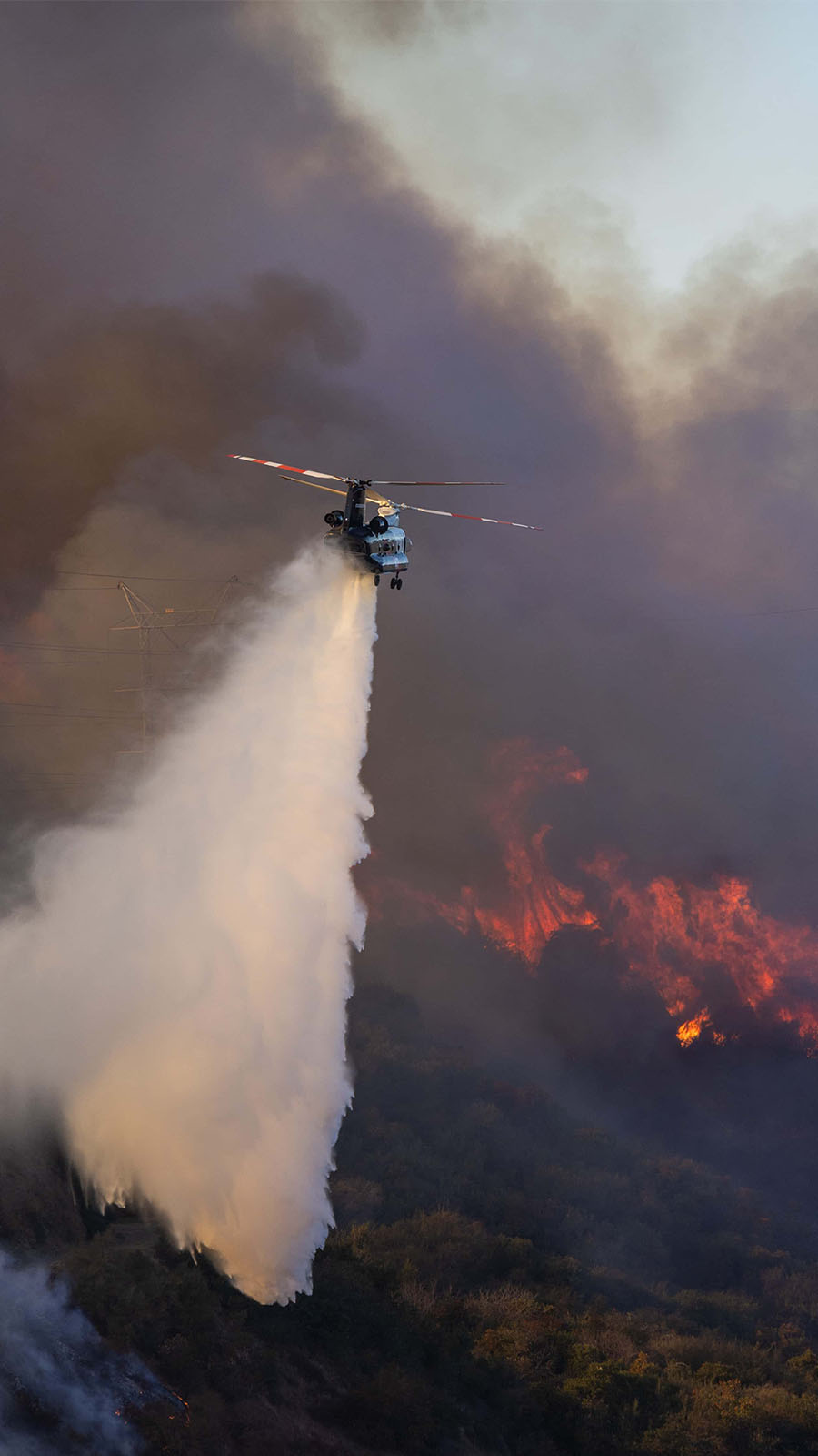 An LA County Fire watering dropping helicopter drops on the Palisades Fire, along Mandeville Canyon, 11 January, 2025