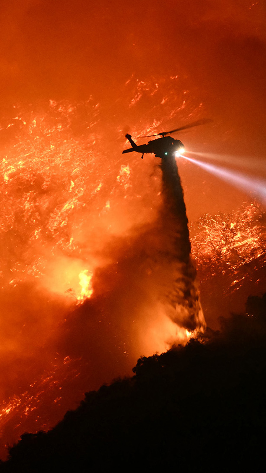 A fire fighting helicopter drops water as the Palisades fire grows near the Mandeville Canyon neighborhood