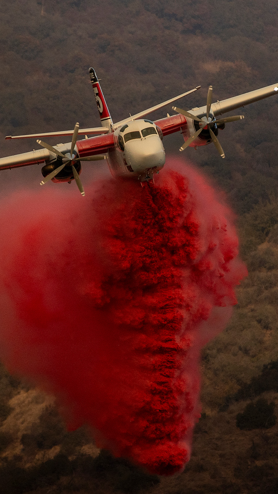 A Cal Fire S-2T firefighting tanker releases retardant while battling the Palisades Fire in the Mandeville Canyon neighborhood