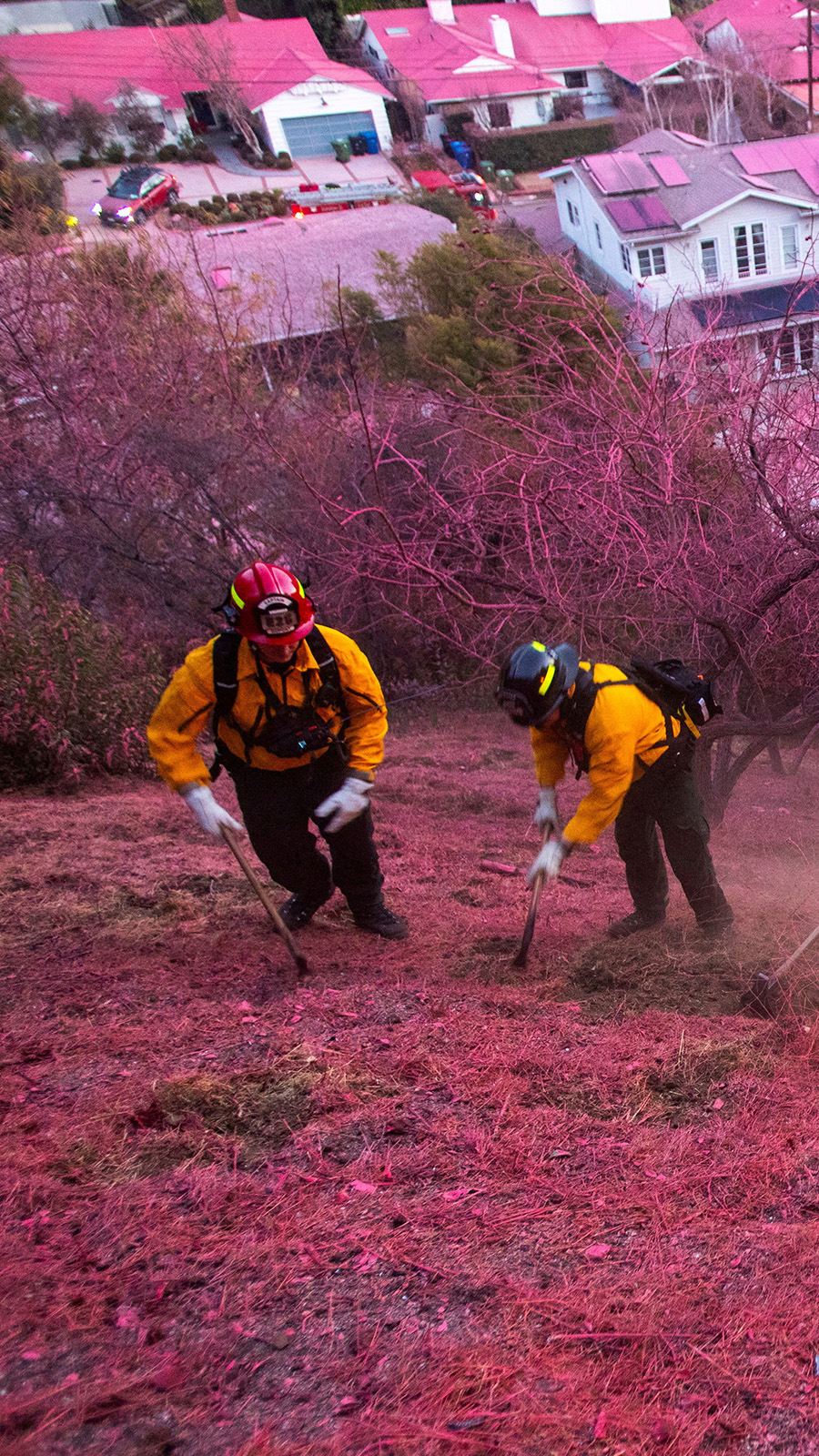 Firefighters work to clear a firebreak on a hillside covered with retardant as the Palisades Fire