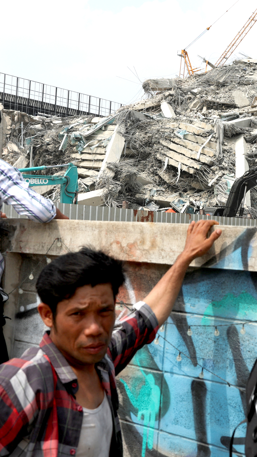 Migrant workers wait at the site of the collapsed building.