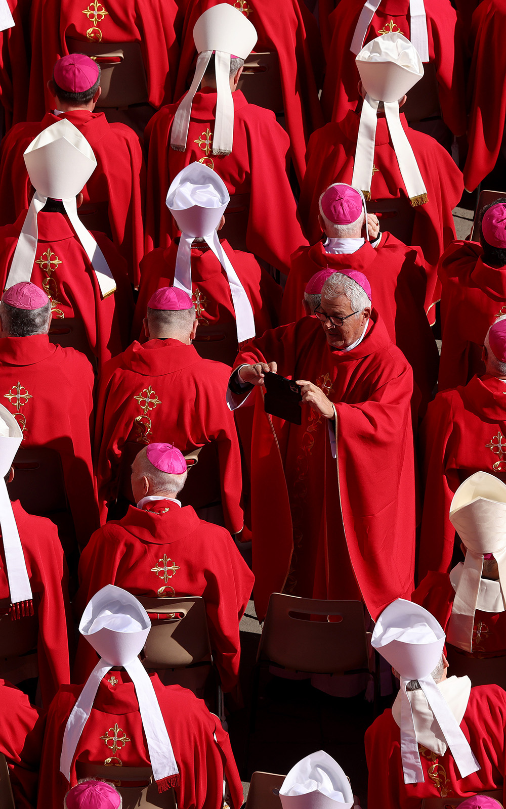 Bishop takes a photo of cardinals and bishops dressed in red robes, white mitres and purple caps