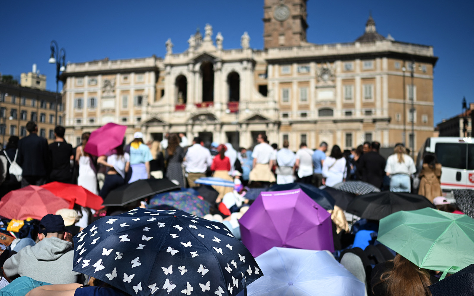 Attendees, holding umbrellas of different colours to protect them from the sun, wait in front of Santa Maria Maggiore Basilica