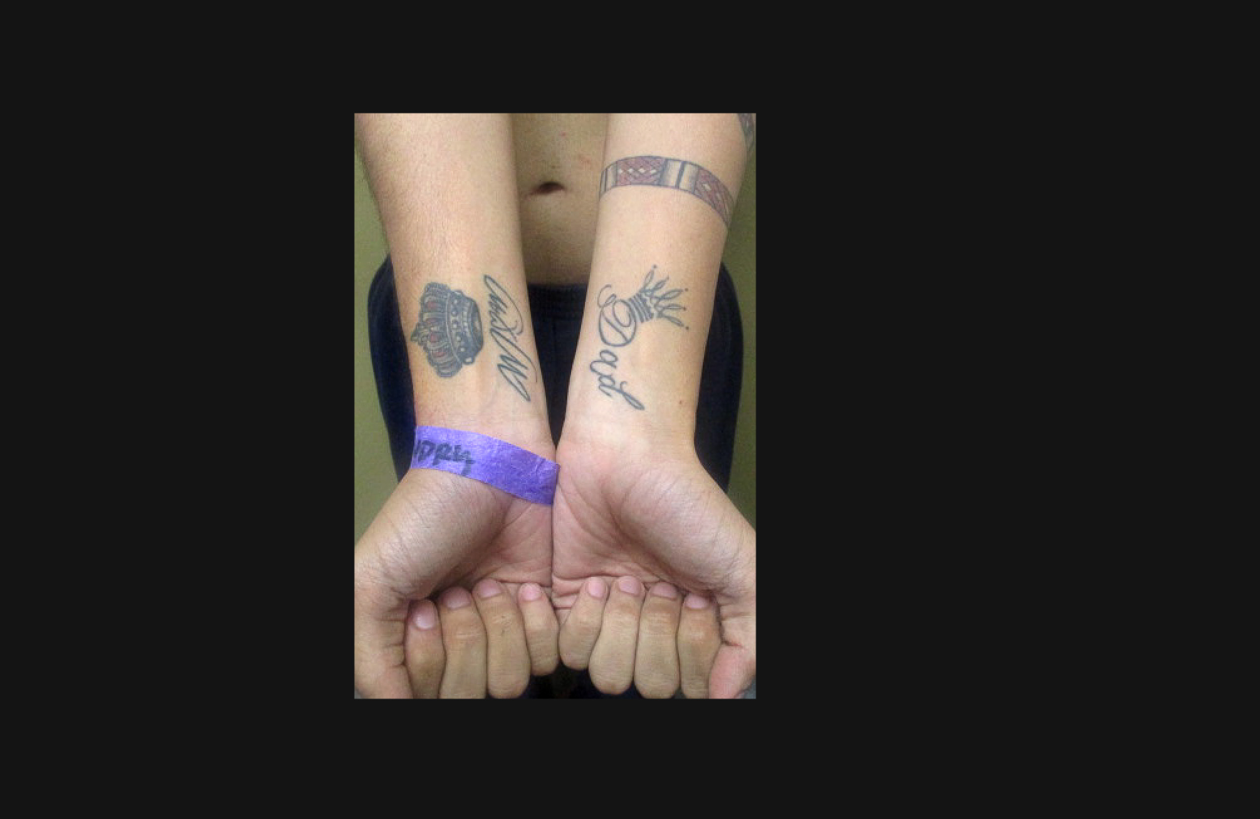 Prisoner holds wrists upwards to show tattoos on forearms of Mom on one arm and Dad on the other, with a crown above each