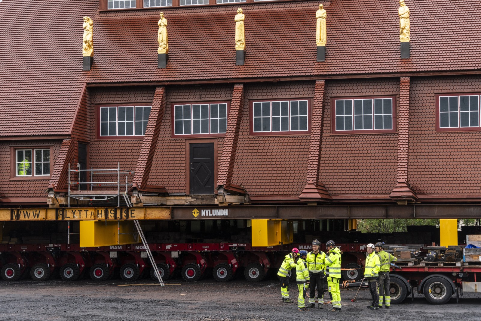 Workers in high-vis outfits and hard hats perform final preparations on the church building, which can be seen on a wheeled structure