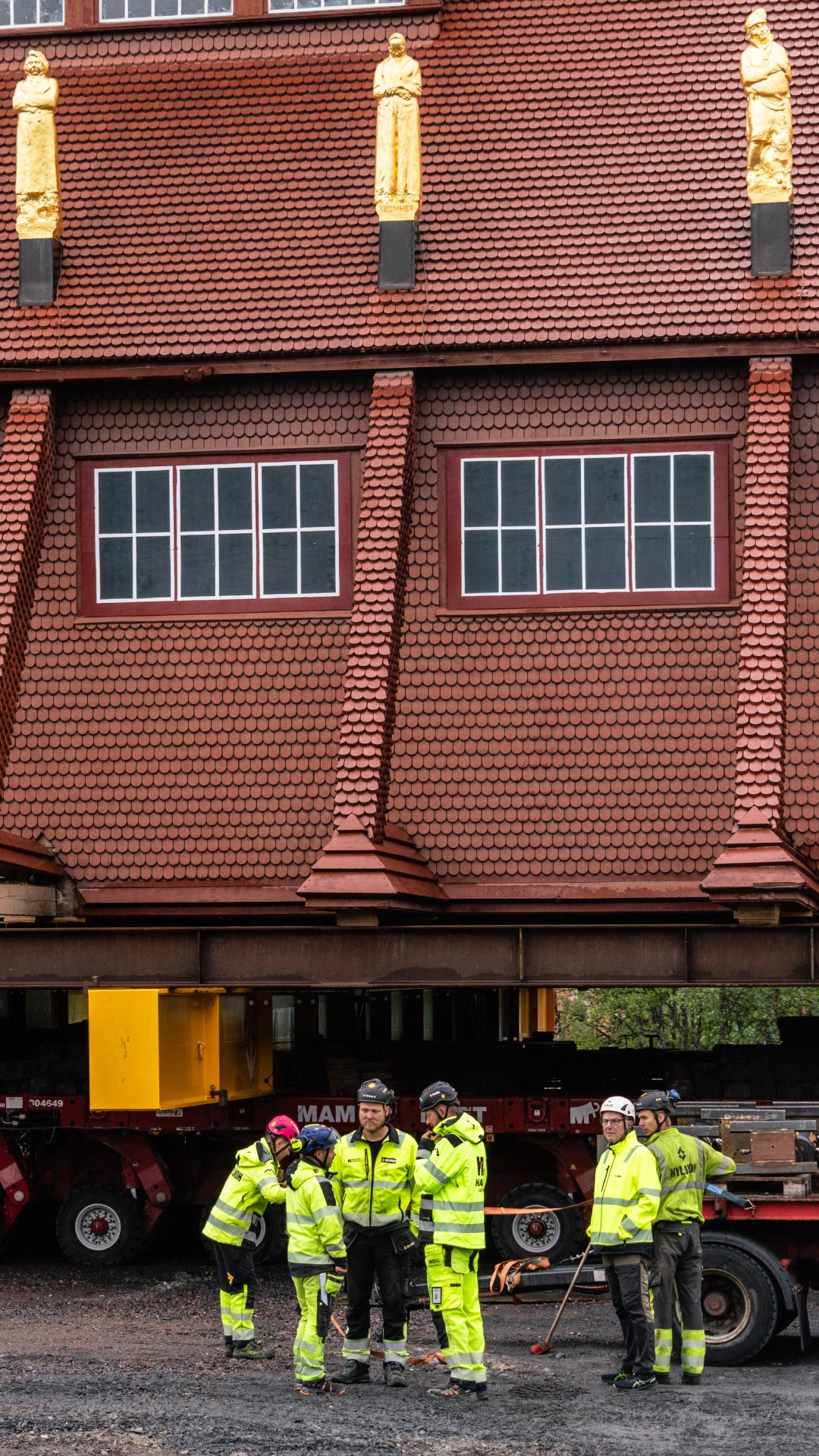 Workers in high-vis outfits and hard hats perform final preparations on the church building, which can be seen on a wheeled structure