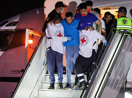 Trabajadores de la Cruz Roja ayudan a bajar del avión a migrantes venezolanos tras su llegada al país luego de estar presos en el Cecot