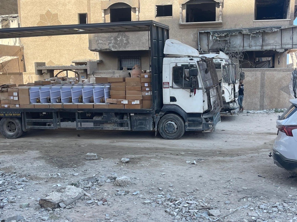 Karton kutular ve beyaz plastik kutularla yüklü bir kamyon enkaz parçaları dolu bir sokakta park halindeyken.