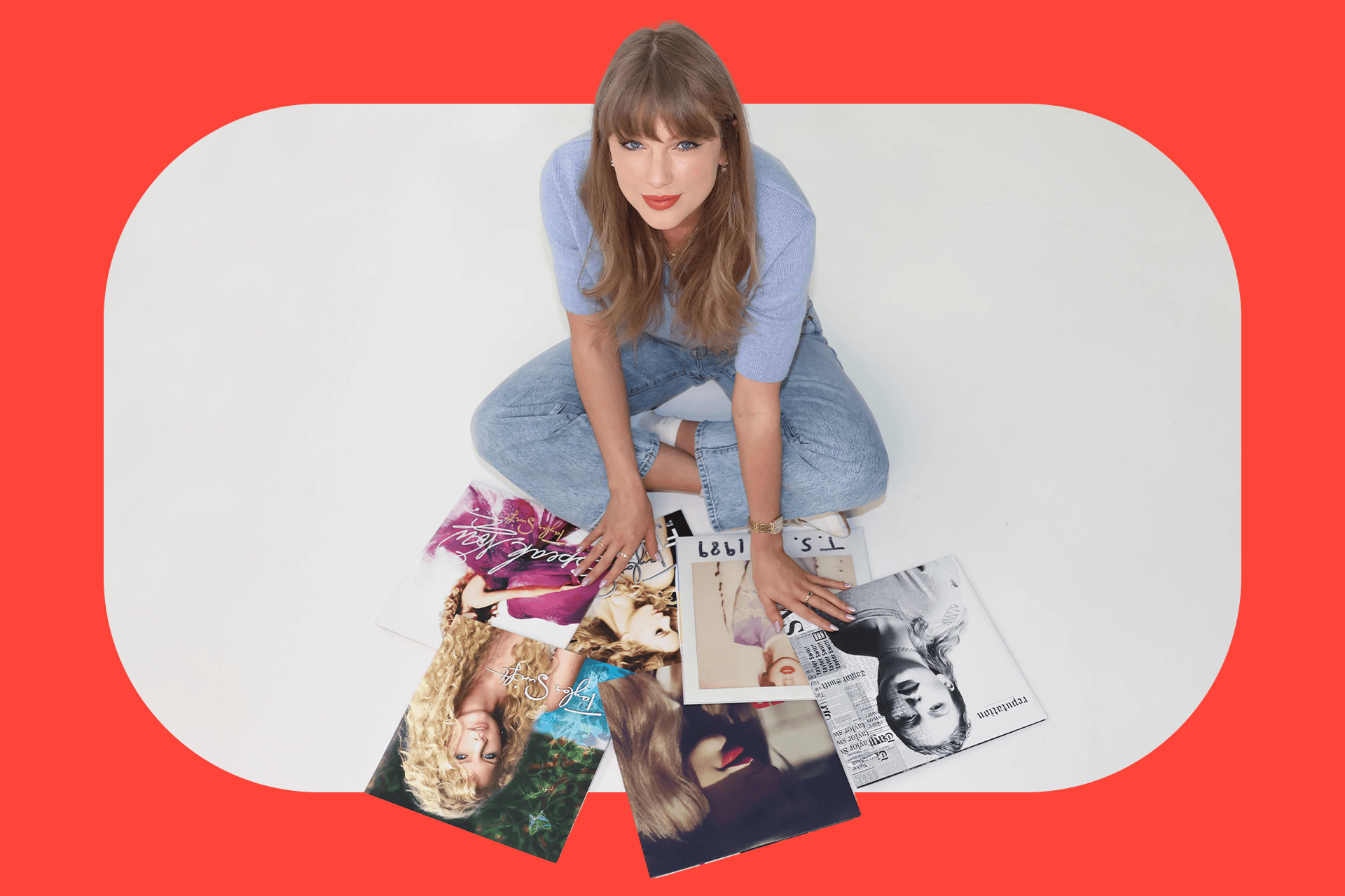 Photo of Taylor Swift, sitting cross-legged, wearing jeans and a light blue sweater and looking at the camera from below, while she sifts through her own albums in vinyl version