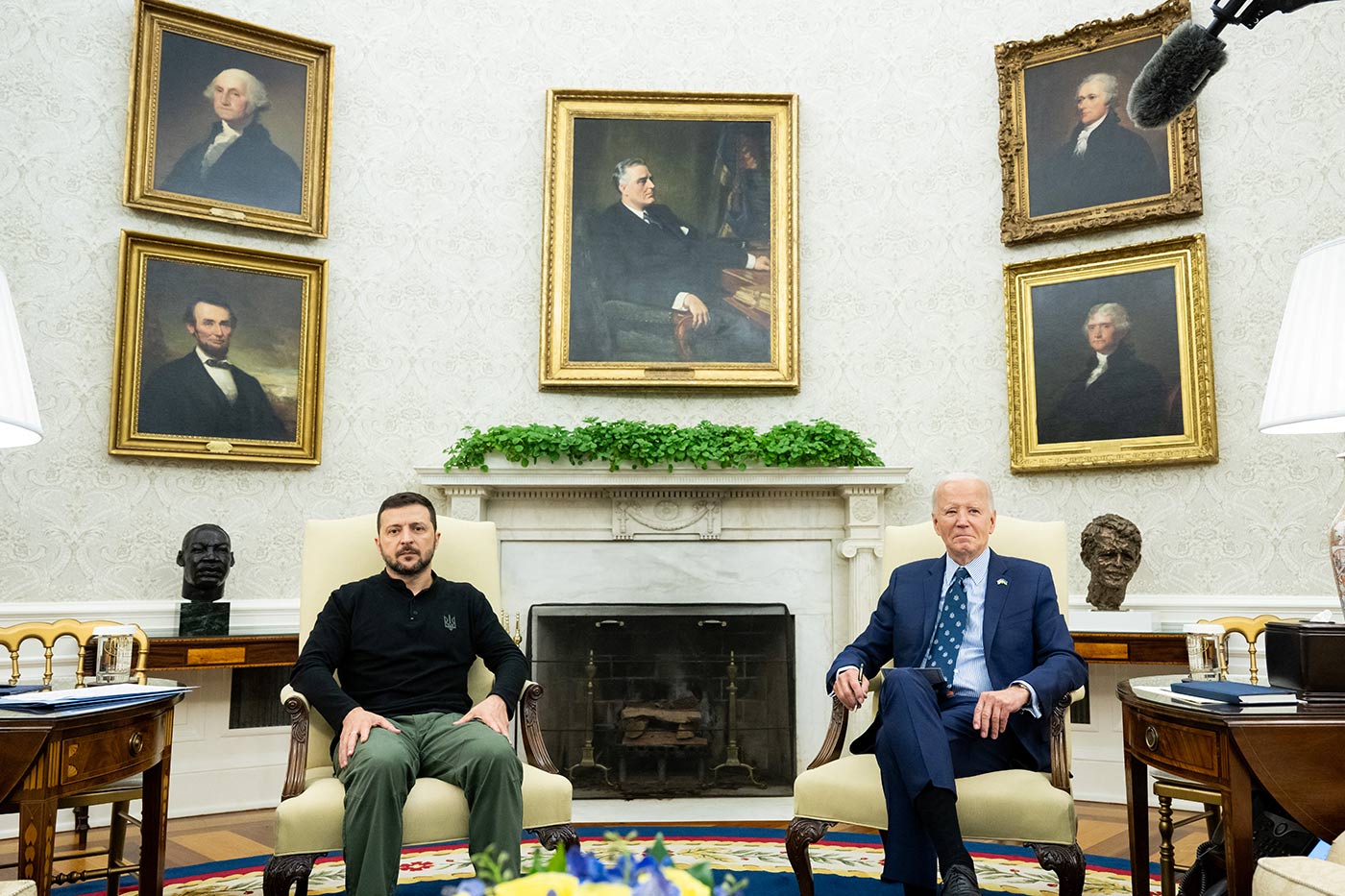 Joe Biden takohet me Presidentin ukrainas Volodymyr Zelensky në Zyrën Ovale, me të dy burrat të ulur në kolltuqe ngjyrë kremi përpara një oxhaku të bardhë. Dhoma ka mure ngjyrë kremi të zbukuruara me pesë portrete të mëdha të figurave historike të rregulluara në mënyrë simetrike. Një bimë e gjelbër qëndron në oxhak mbi oxhak, dhe një qilim shumëngjyrësh me një dizajn të vulës presidenciale mbulon dyshemenë. Tavolina anësore prej druri me llamba dhe dokumente shoqërojnë karriget.