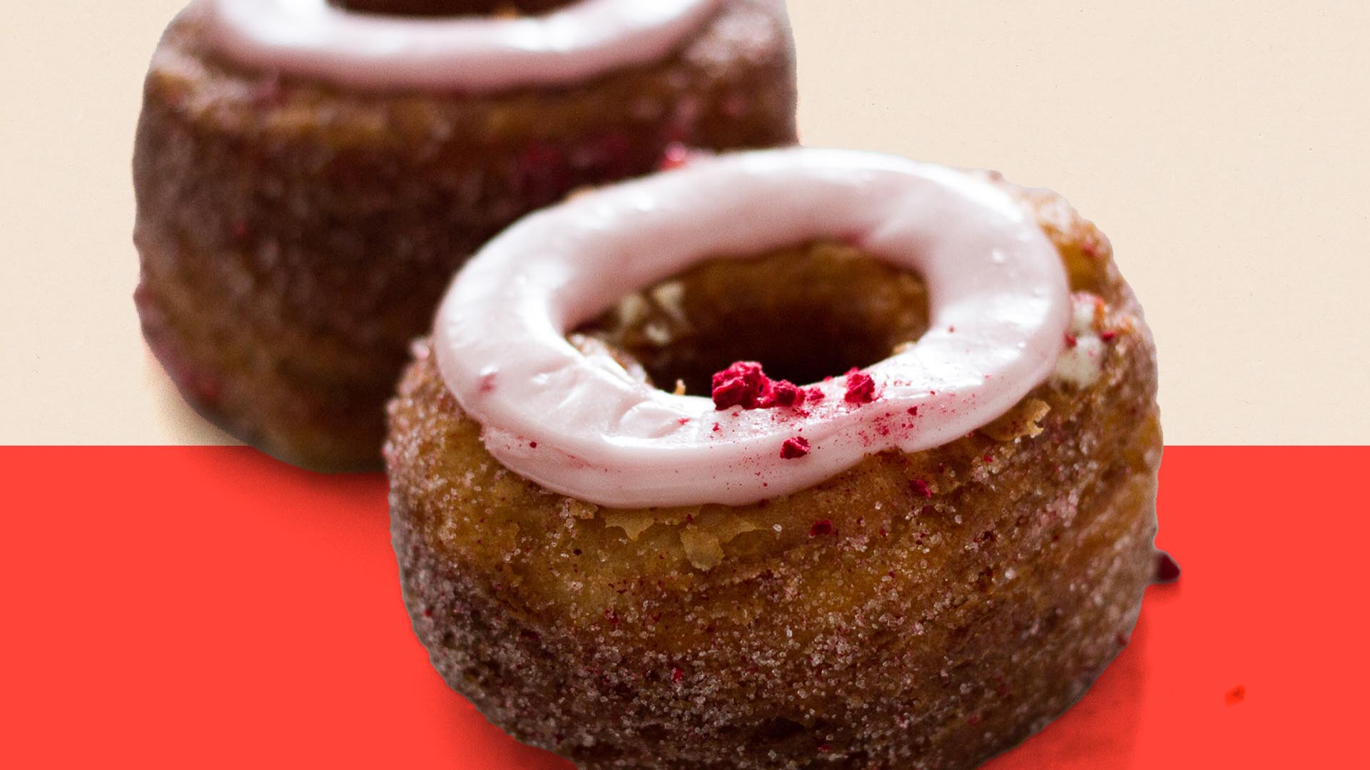 A close up of a cronut, a cross between a croissant and a donut. The icing is light pink and the cronut is a dark brown.