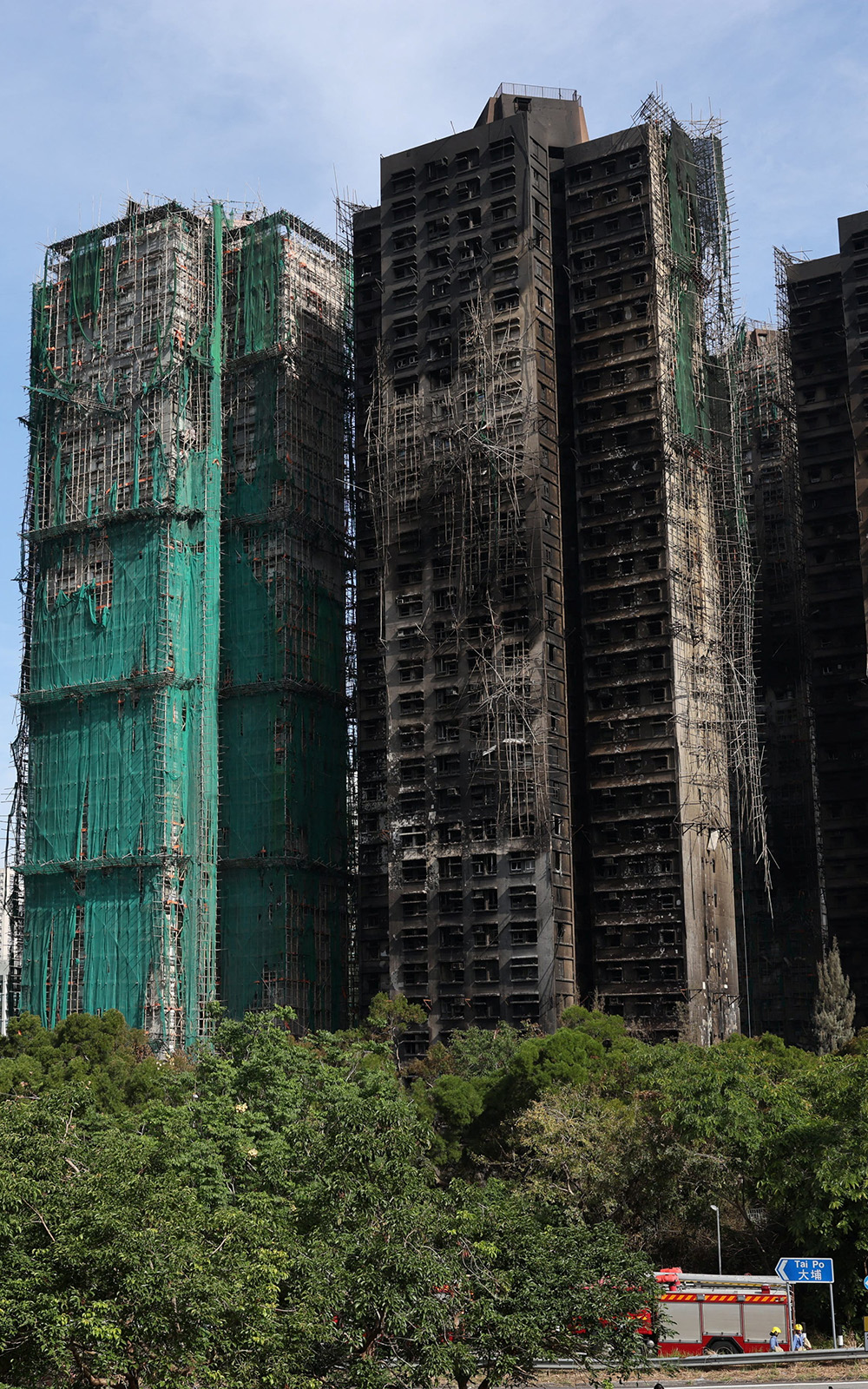 Blackened towers of Wang Fuk Court after the fire. Some of the towers still have scaffolding and green net meshing draped on them