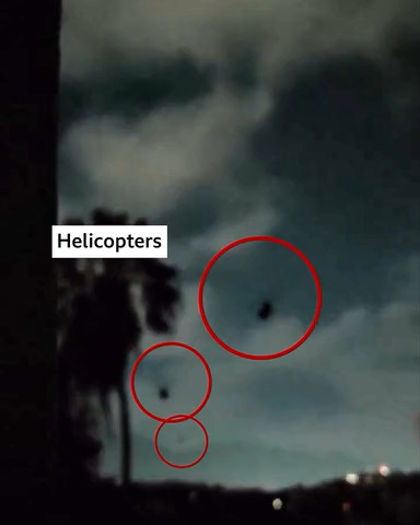 Nighttime scene with a cloudy sky and silhouettes of palm trees. Three helicopters are visible in the sky, each circled in red for emphasis